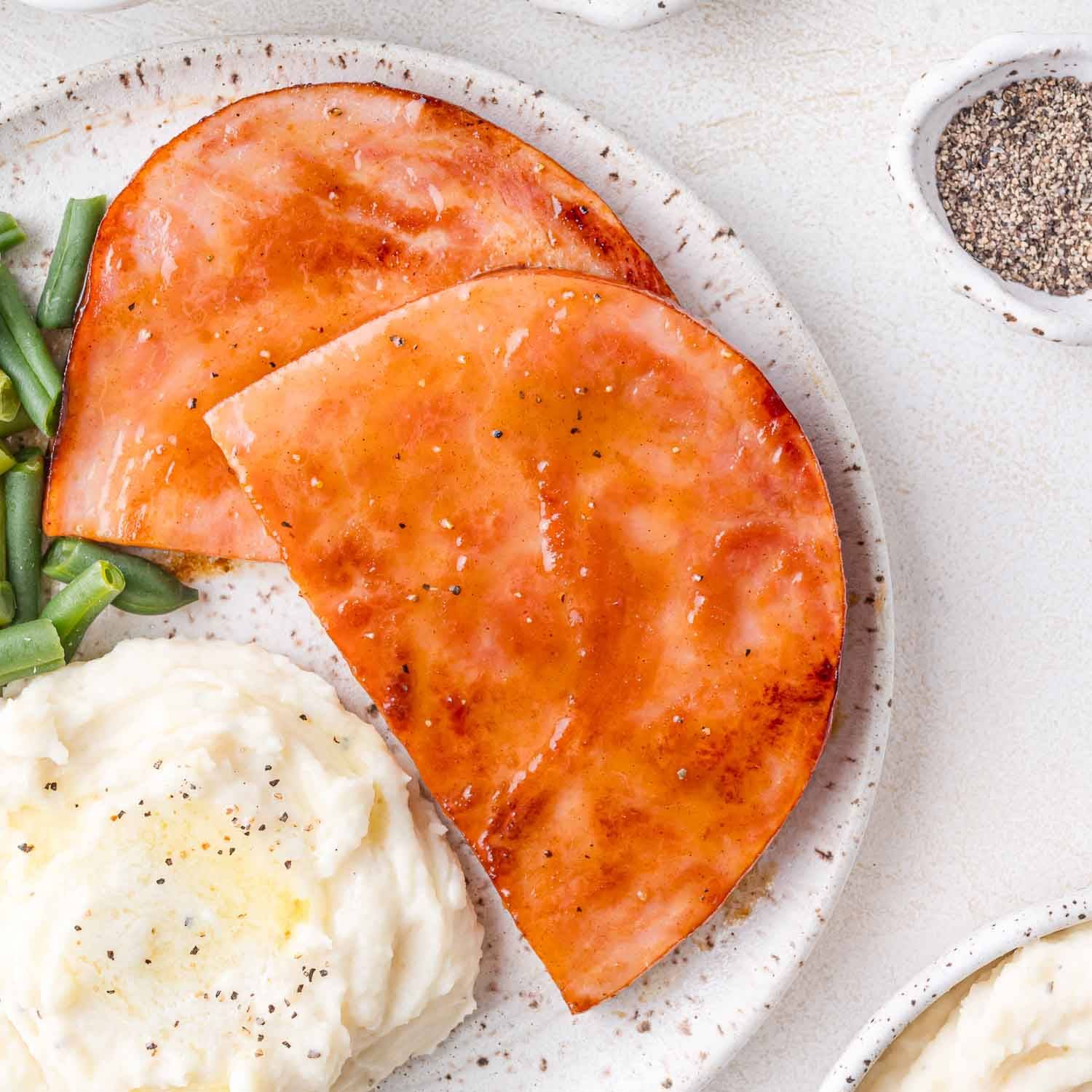 Ham steak on a plate with mashed potatoes.