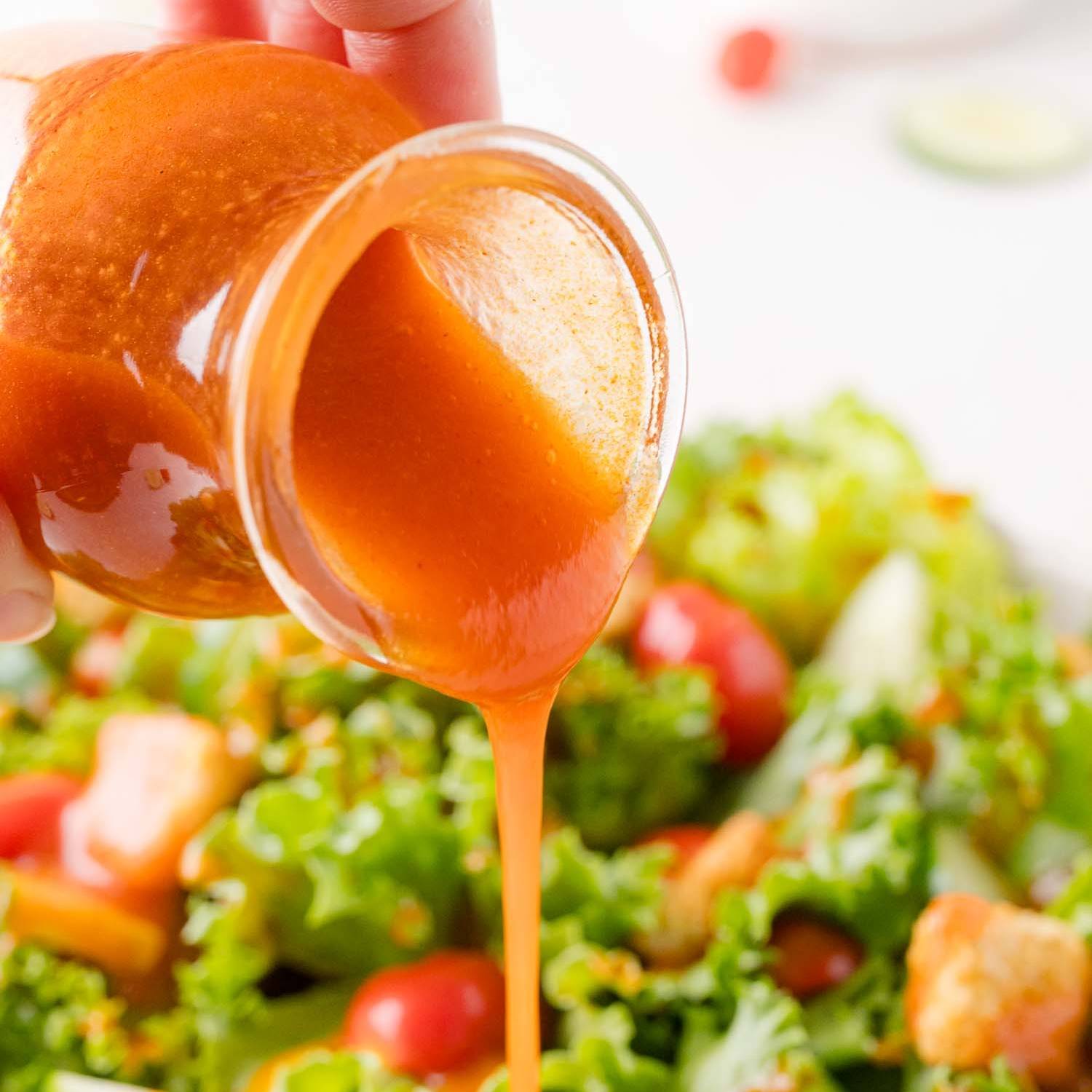Homemade Catalina dressing being poured on a leafy green salad.