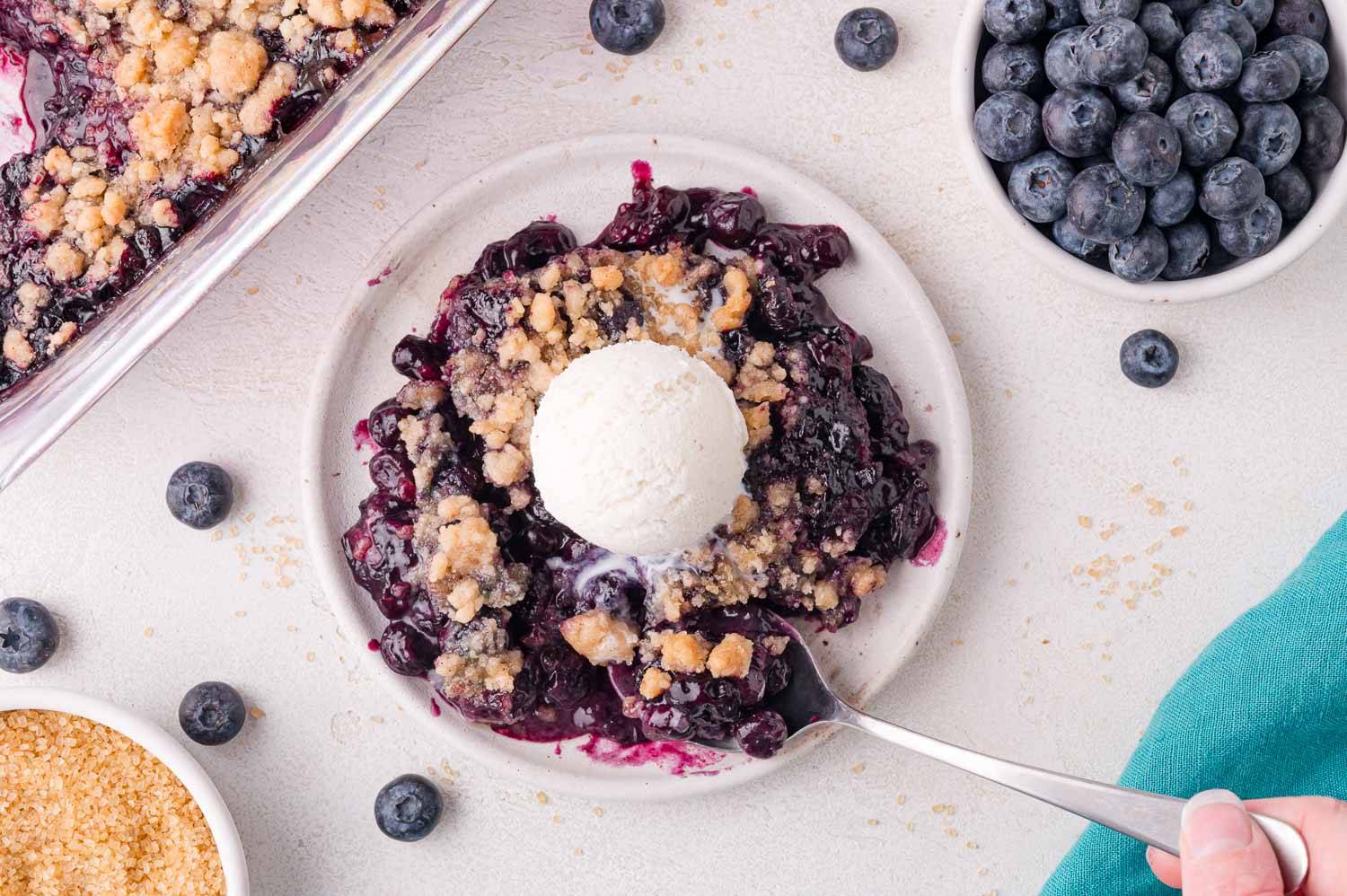 Blueberry crumble on a white plate topped with ice cream.