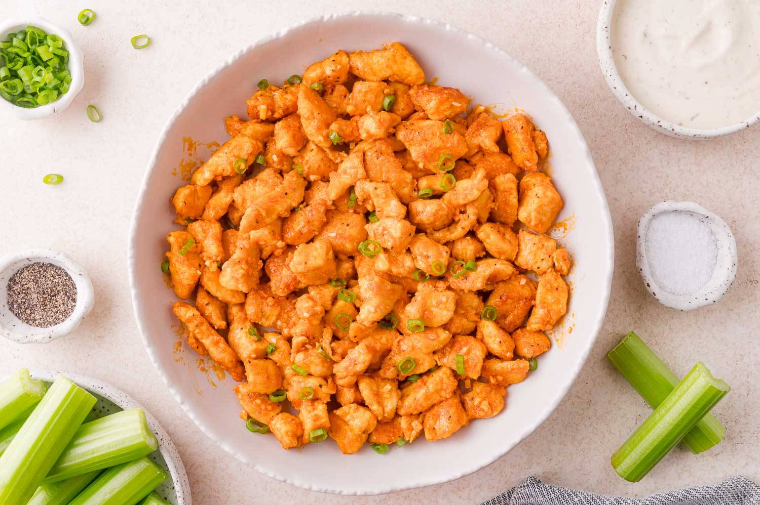 Buffalo chicken bites in a bowl, topped with sliced green onions.