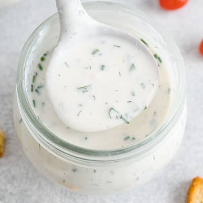 Ranch dressing in a small jar, some being lifted out with a ladle.