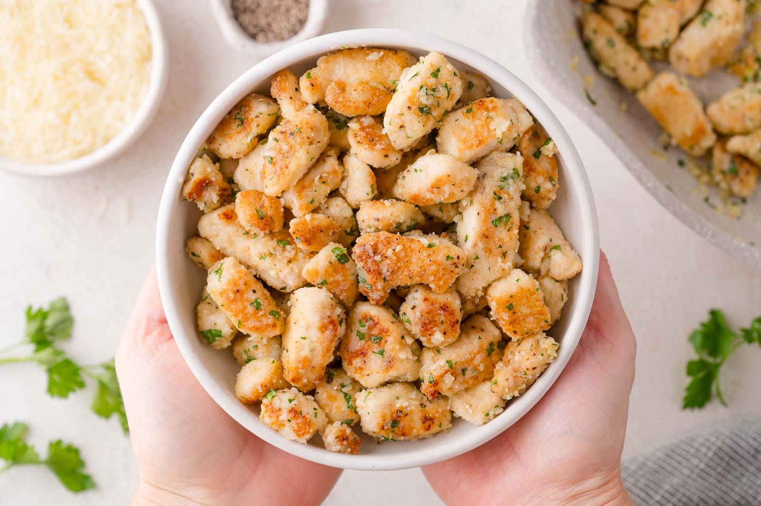Garlic parmesan chicken bites in a white bowl, held with two hands.