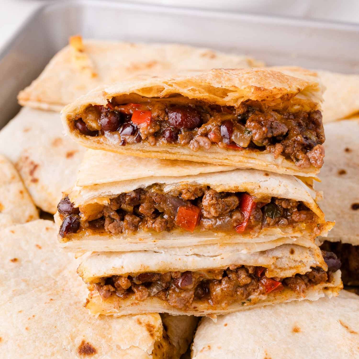 Stack of slices of sheet pan quesadilla, with beef, beans, and peppers visible.