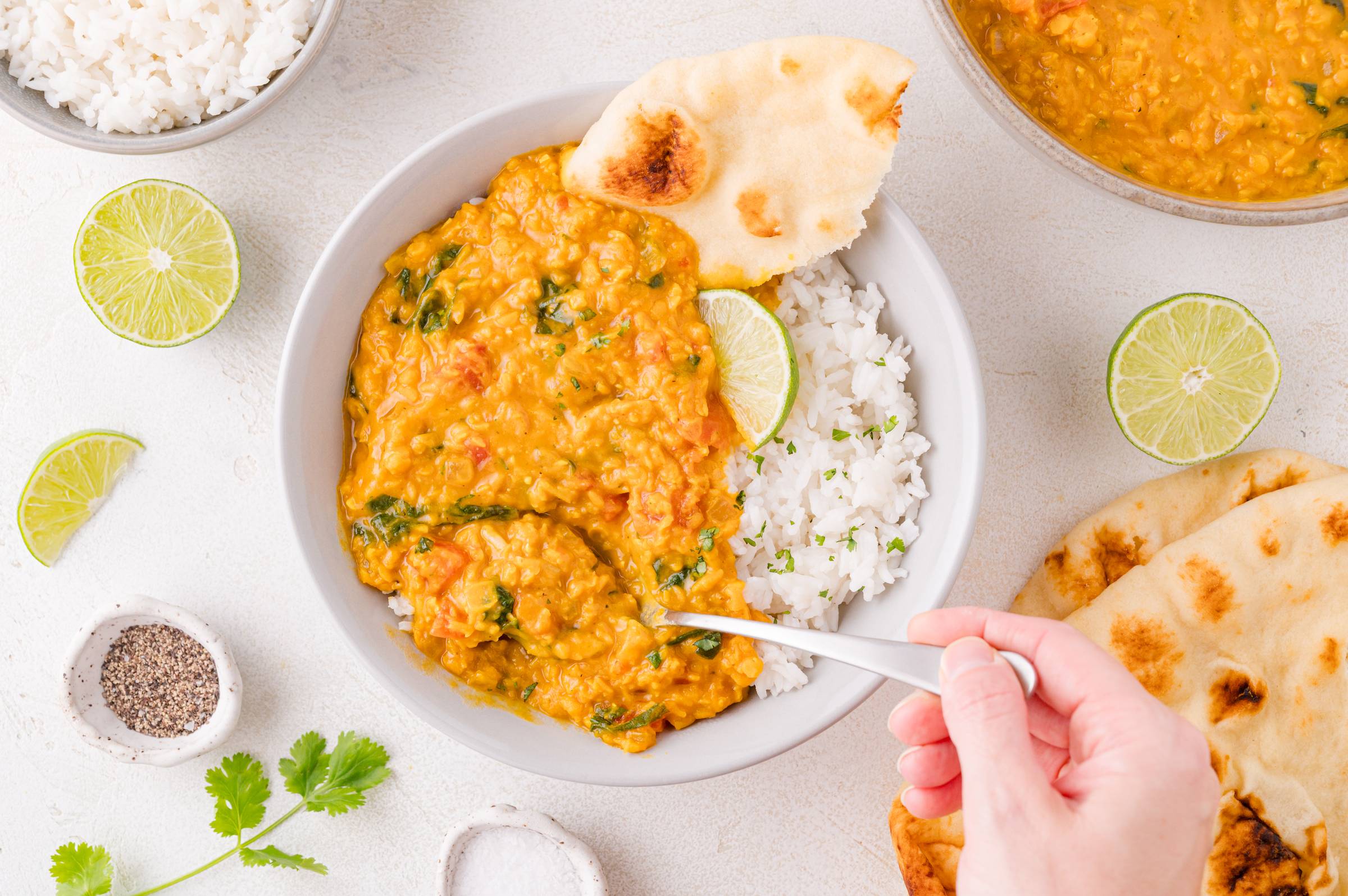 Red lentil curry served with rice and naan, a hand getting a spoonful with a spoon.