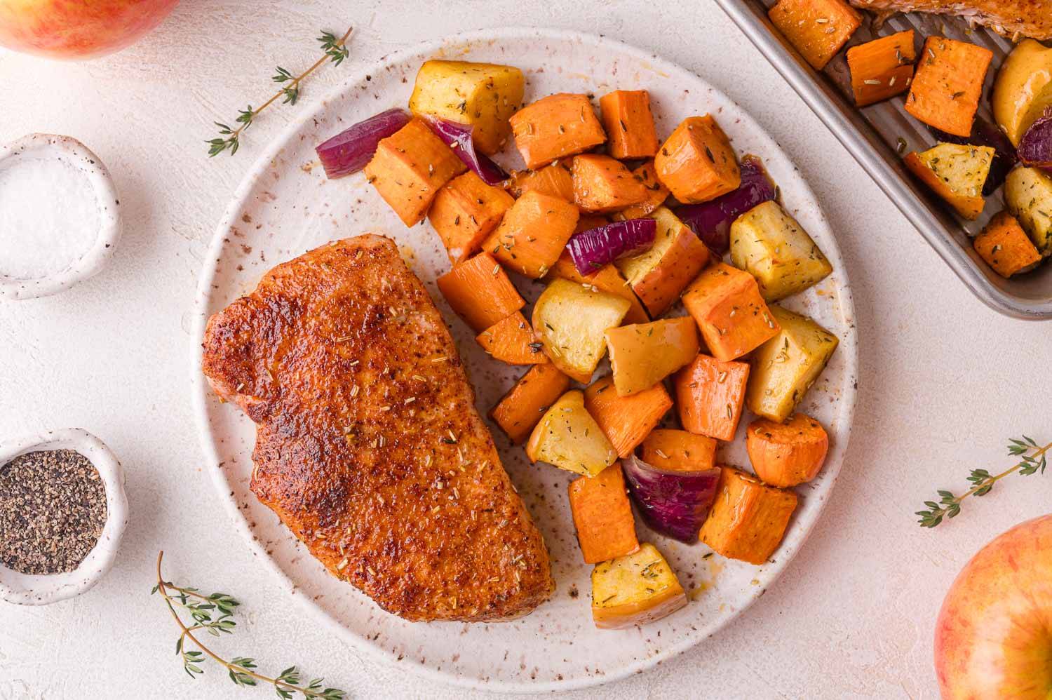 Seasoned pork chop on a plate with apples, sweet potatoes, and onions.