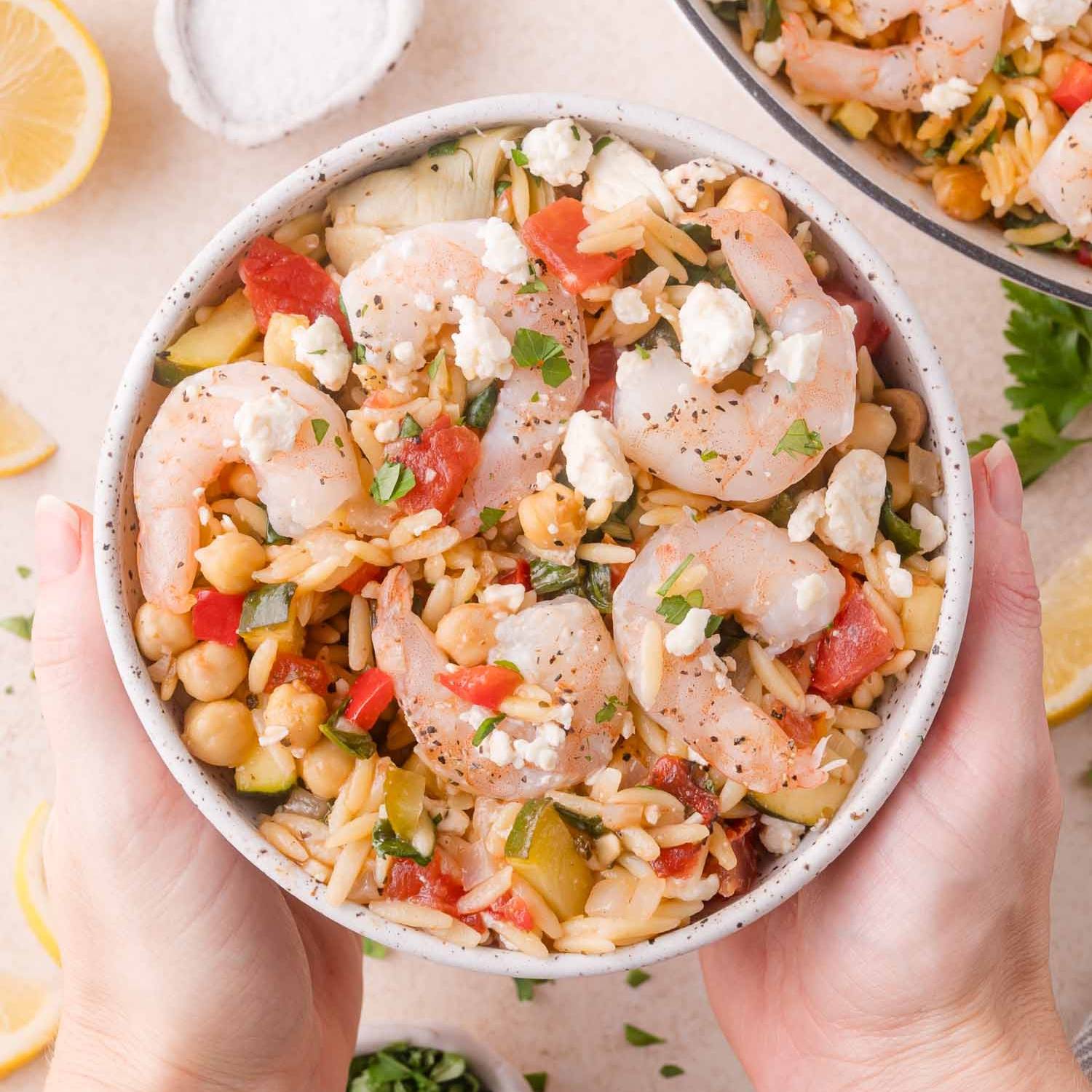 Orzo, chickpeas, and vegetables in a bowl, topped with shrimp and feta.
