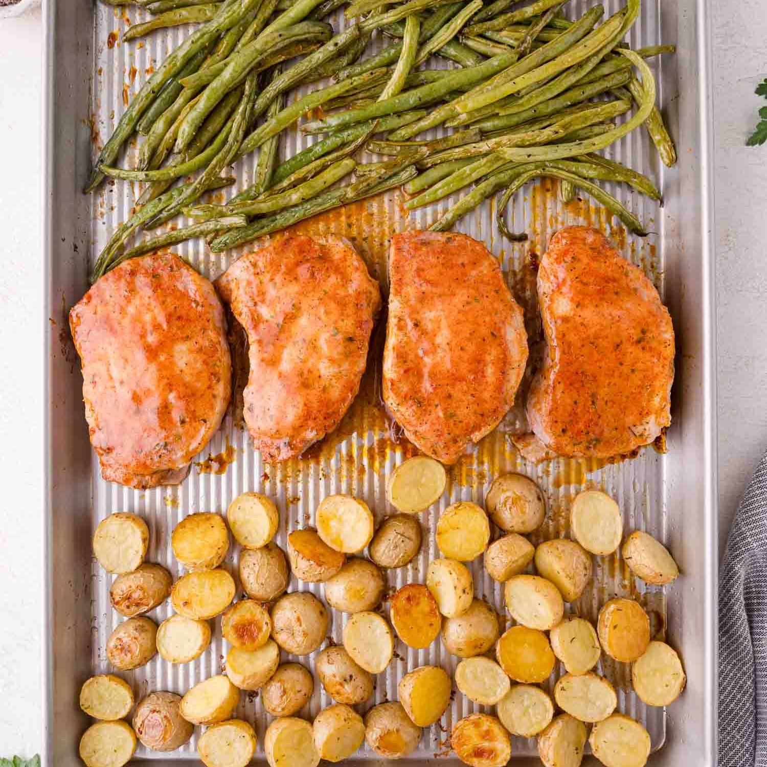 Pork chops, potatoes, and green beans on a sheet pan.
