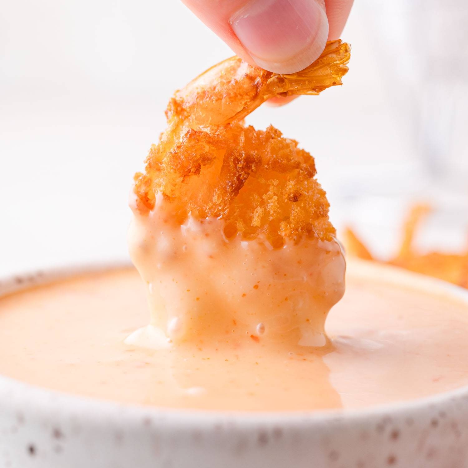 Breaded shrimp being dipped into bang bang sauce.