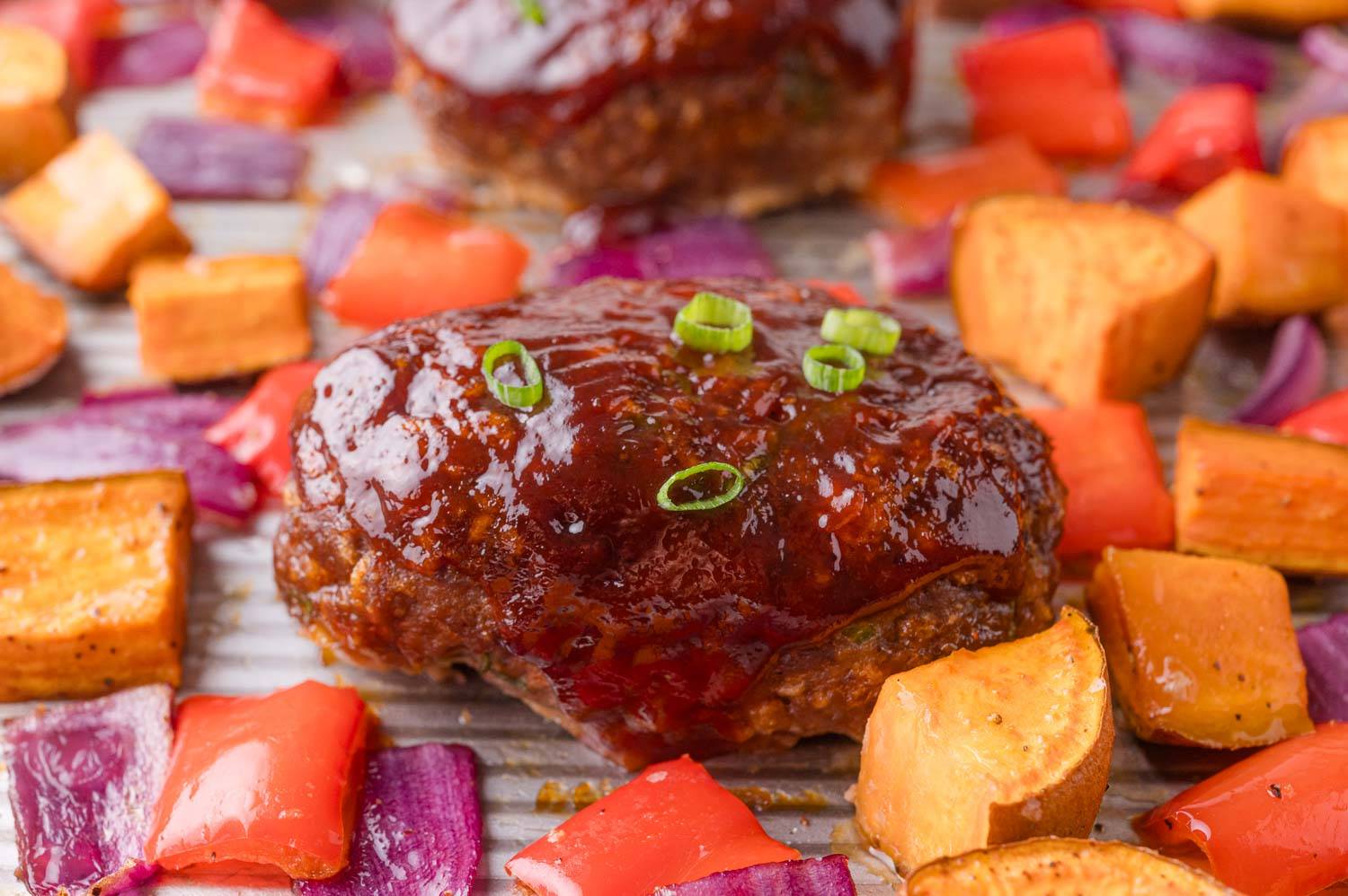Mini bbq meatloaf on a sheet pan with sweet potatoes, bell peppers, onion.