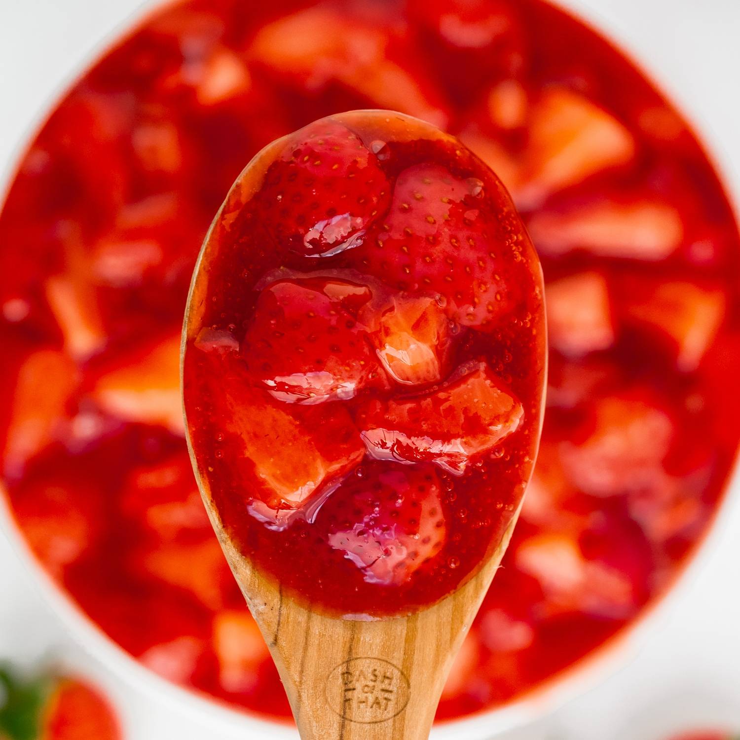 Strawberry sauce in a wooden spoon, held over more sauce.
