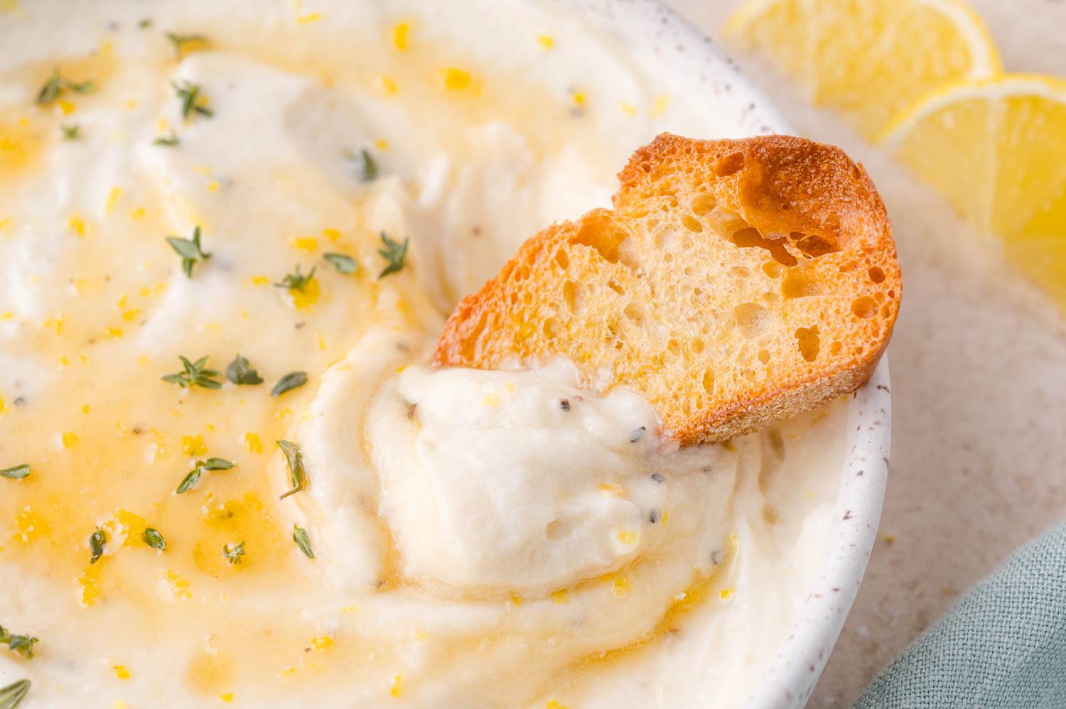 Whipped ricotta topped with thyme and honey, with a piece of toasted bread dipped into it.