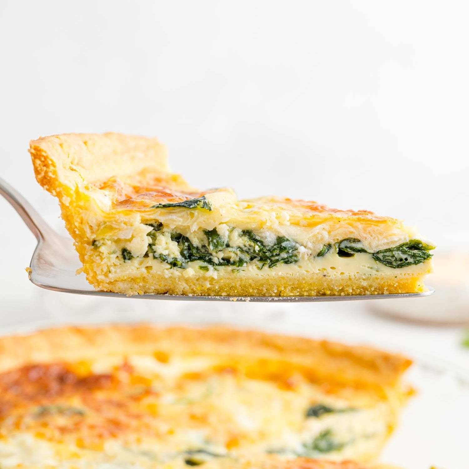 Spinach quiche being lifted wiht a spatula.