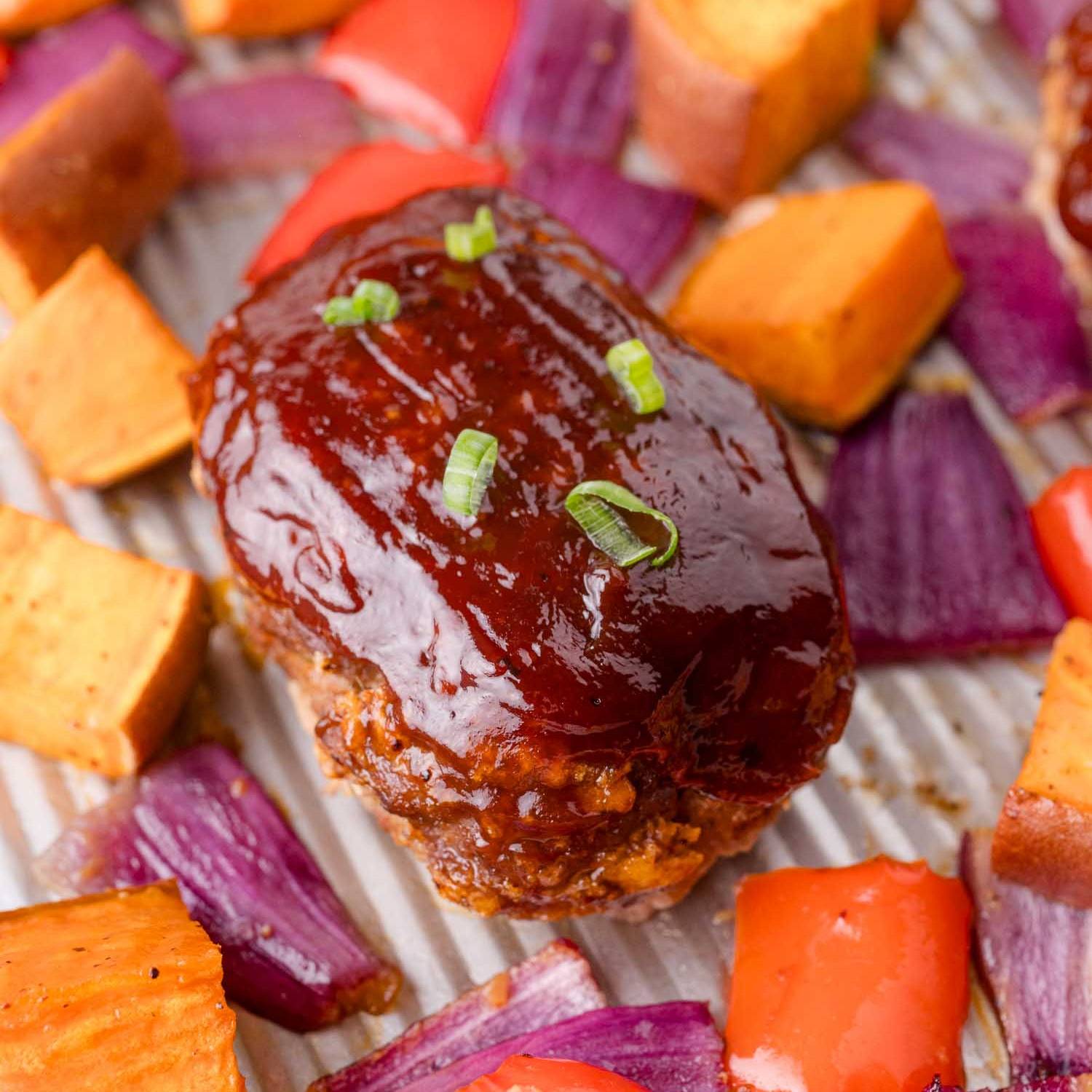 Mini BBQ meatloaf on a sheet pan with sweet potatoes and vegetables.