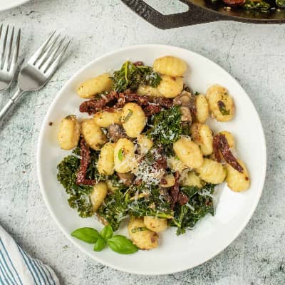 gnocchi, kale, and sun-dried tomatoes in a white bowl.