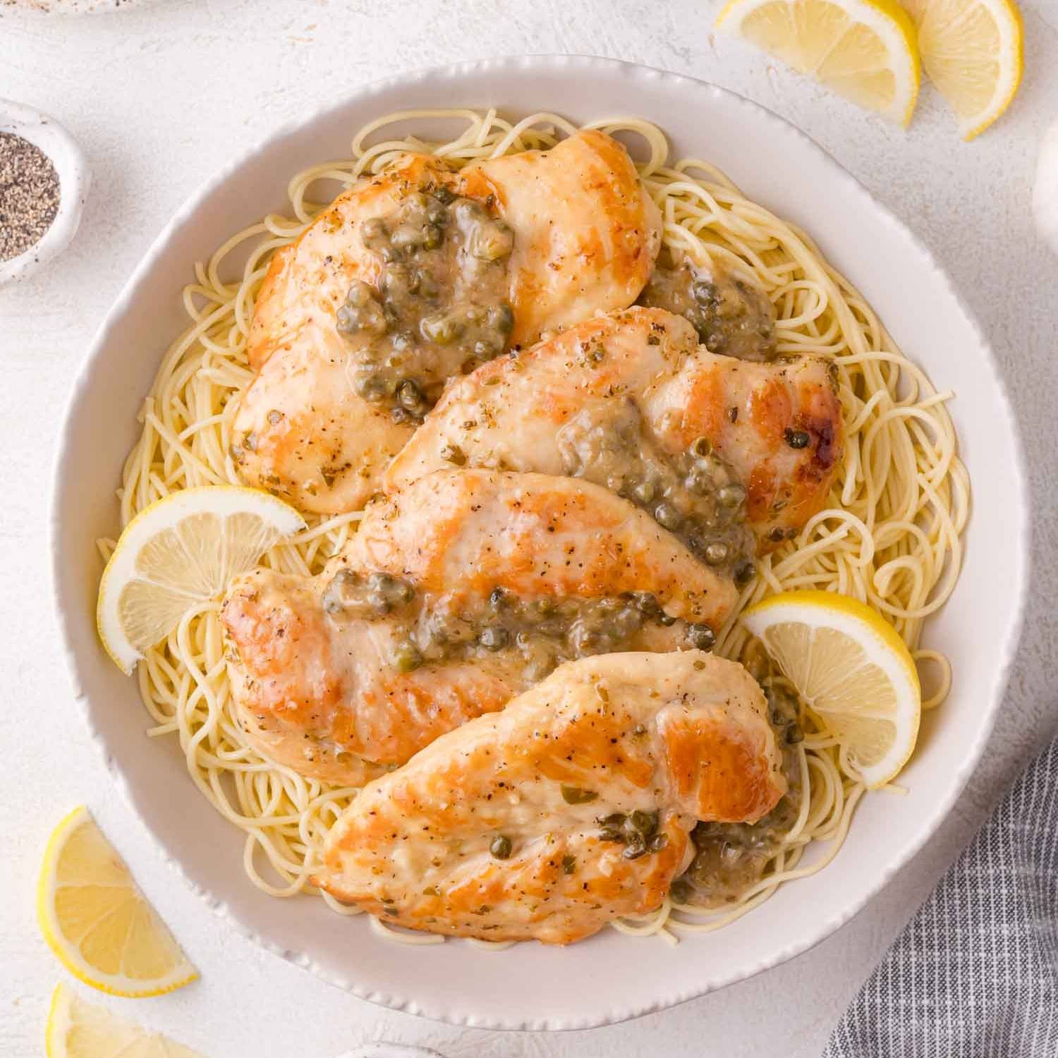 Four pieces of Instant Pot chicken piccata on a plate with angel hair pasta.