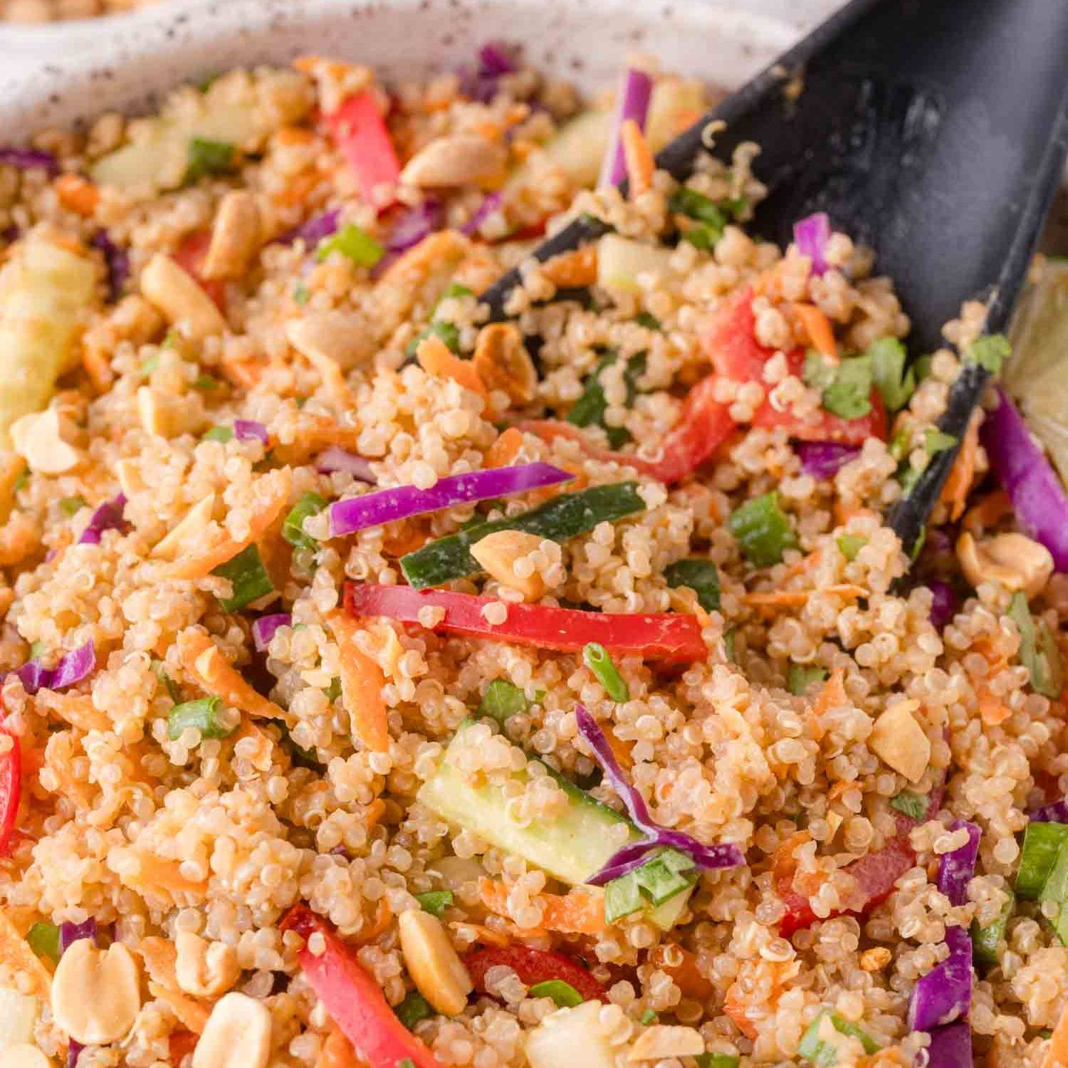 Quinoa with colorful vegetables in a bowl with a black spoon.