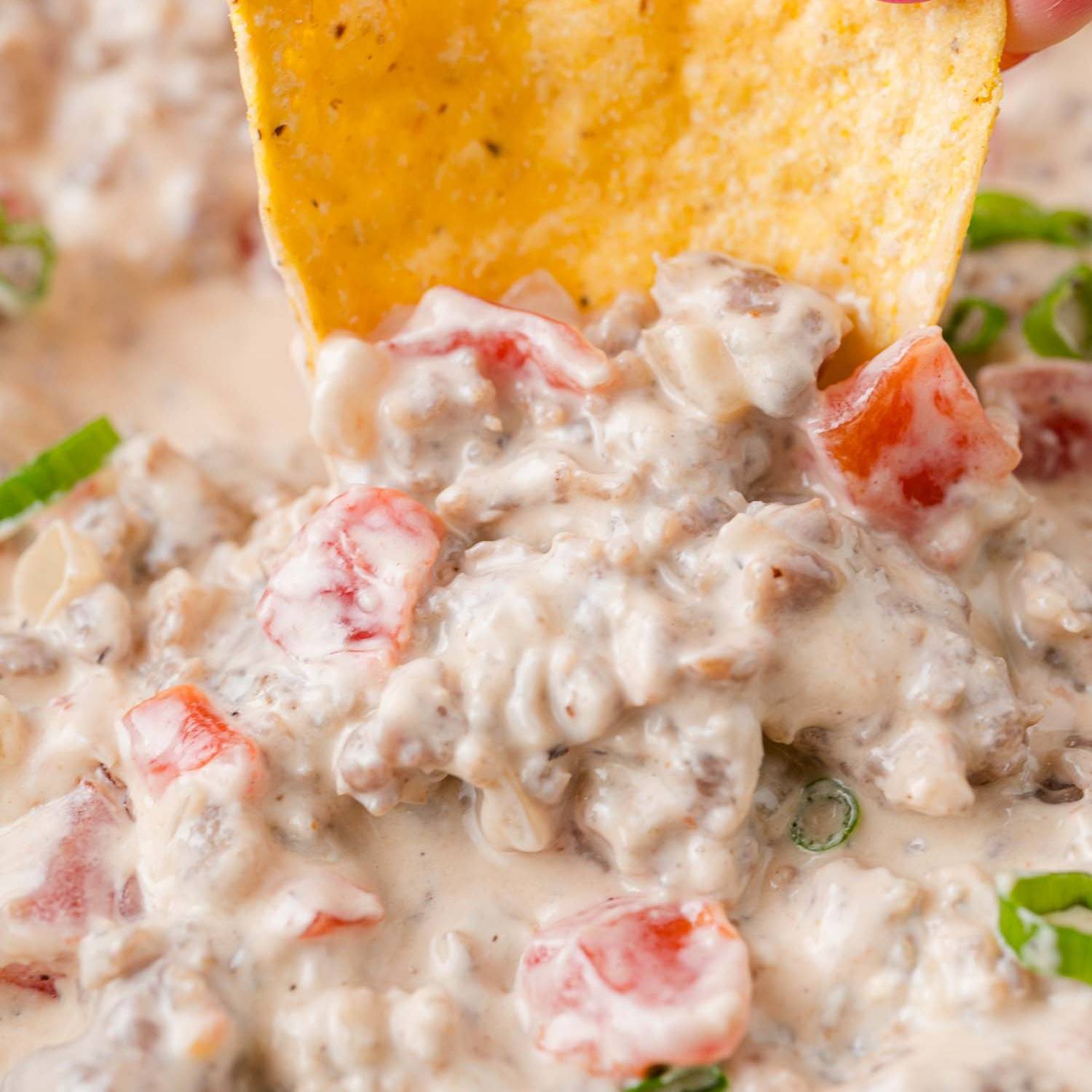 Sausage dip with a chip being dipped into it.