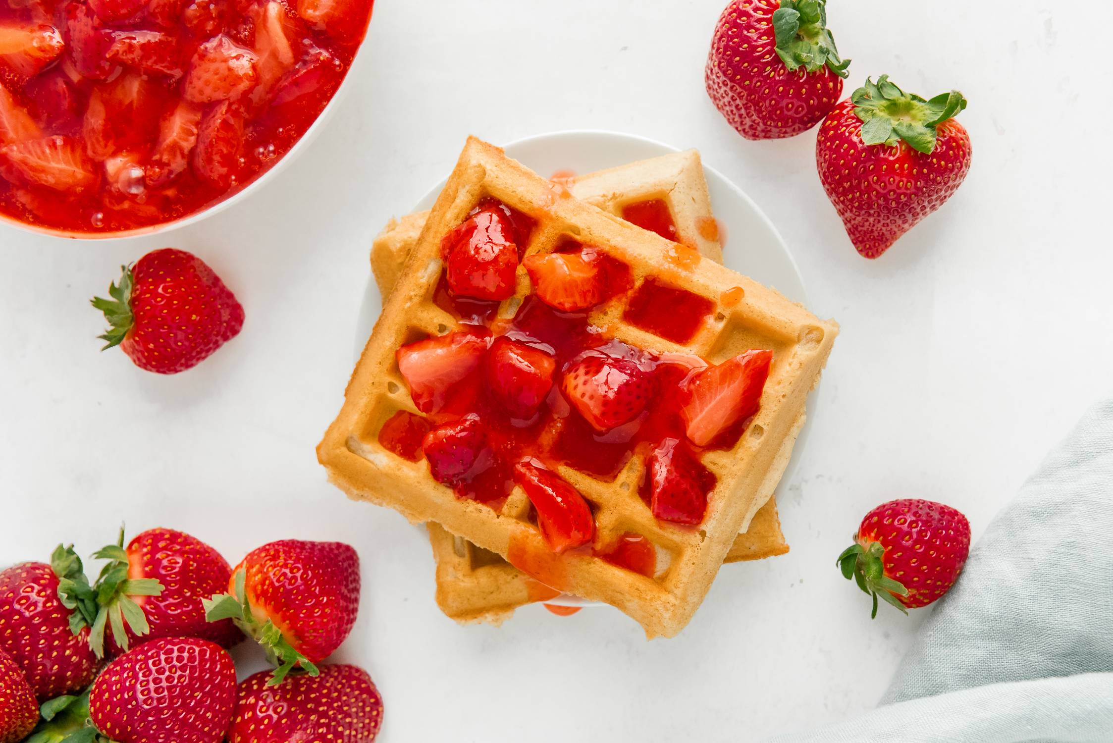 Strawberry sauce on top of waffles, fresh strawberries scattered around.