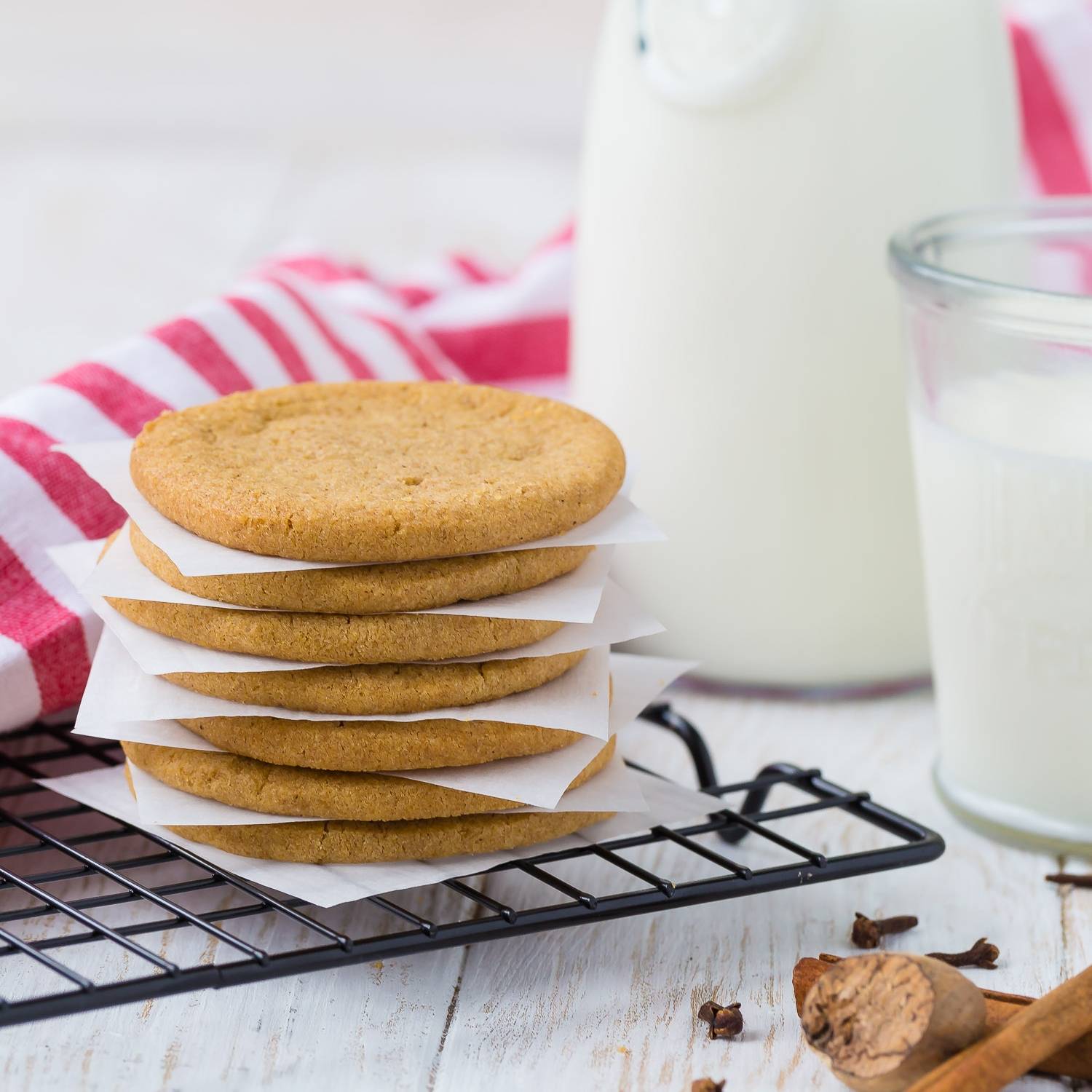 Stacked thin brown cookies, jug of milk in background.