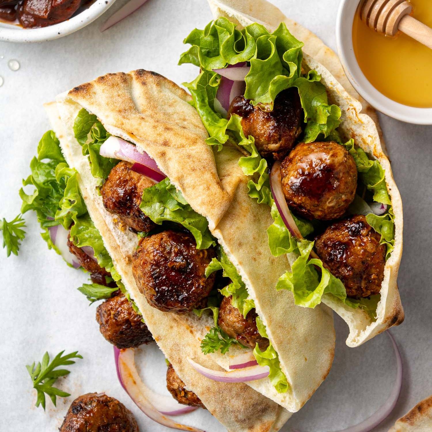 Two pitas with meatballs, lettuce, and onions inside.