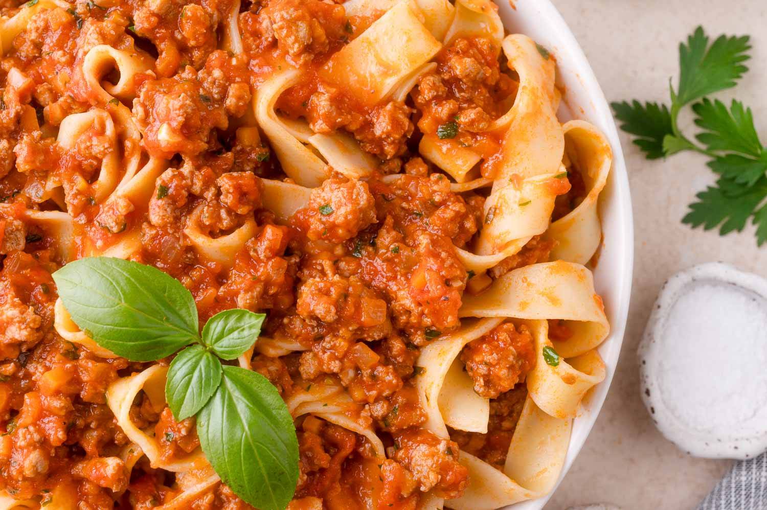 Bolognese sauce on ribbon style pasta, garnished with basil leaves.