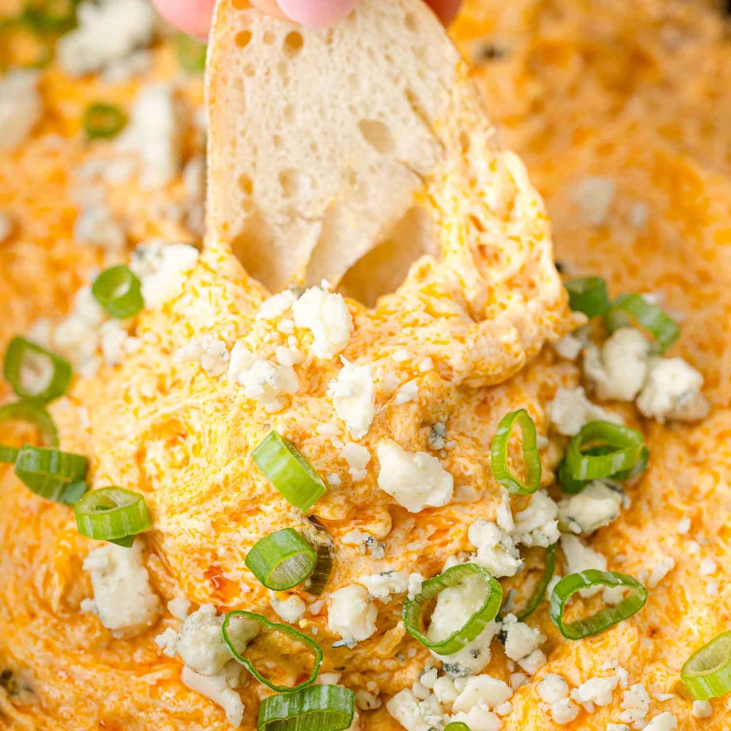 Close up of bread being dipped in crockpot buffalo chicken dip.
