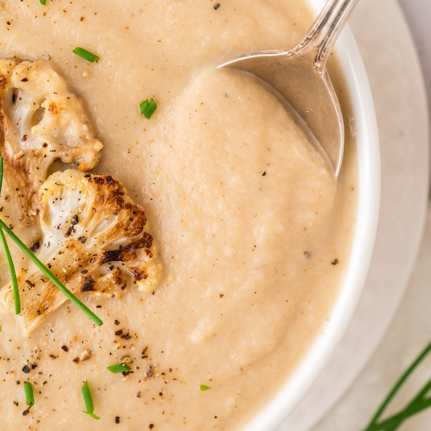 Overhead view of a smooth cauliflower soup, with a spoon in it. 