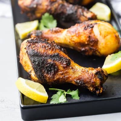 Grilled drumsticks on black platter.