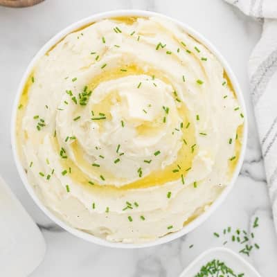 Mashed potatoes in bowl topped with melted butter and chives.