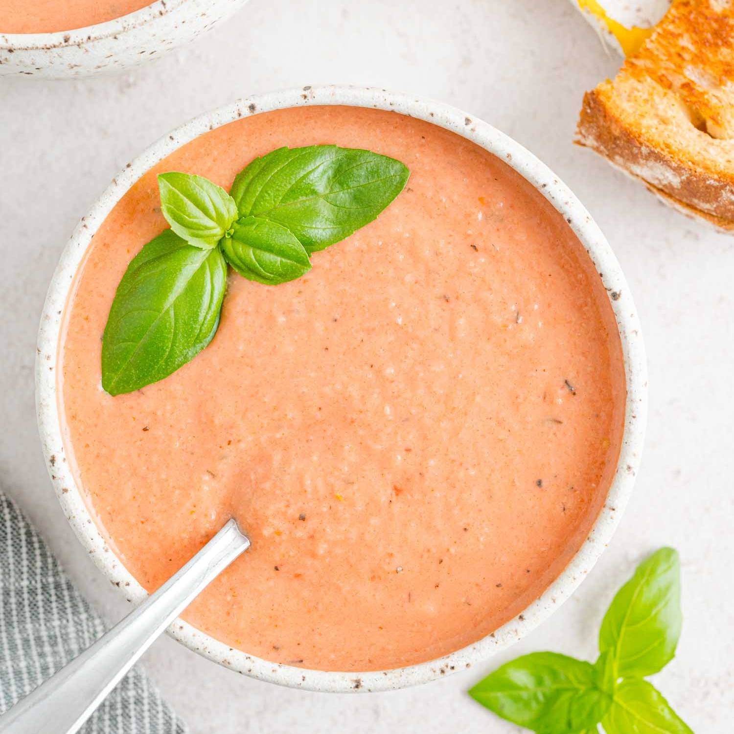 Light colored creamy tomato soup in a bowl topped with fresh basil.