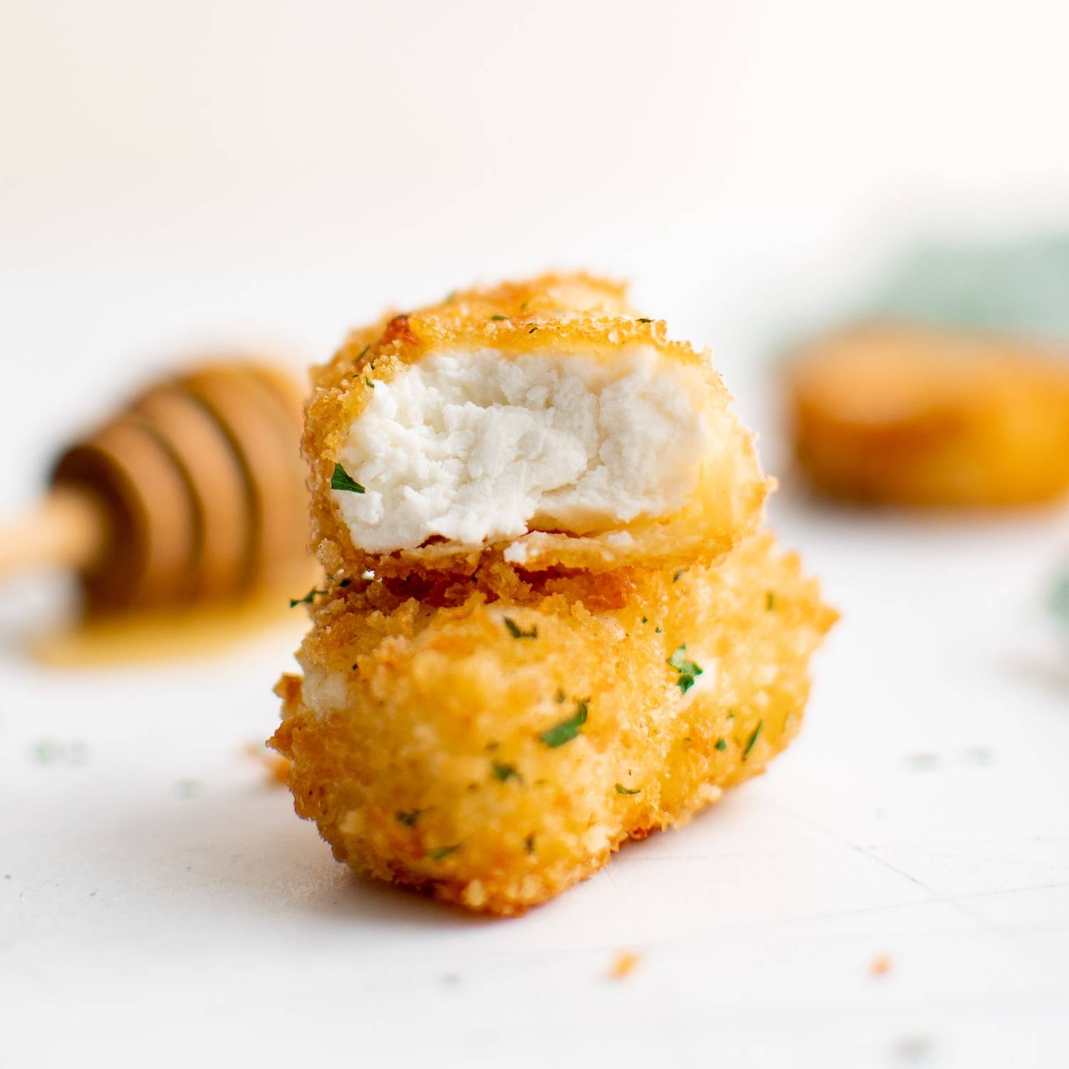 Two pieces of fried goat cheese, one with a bite out of it.