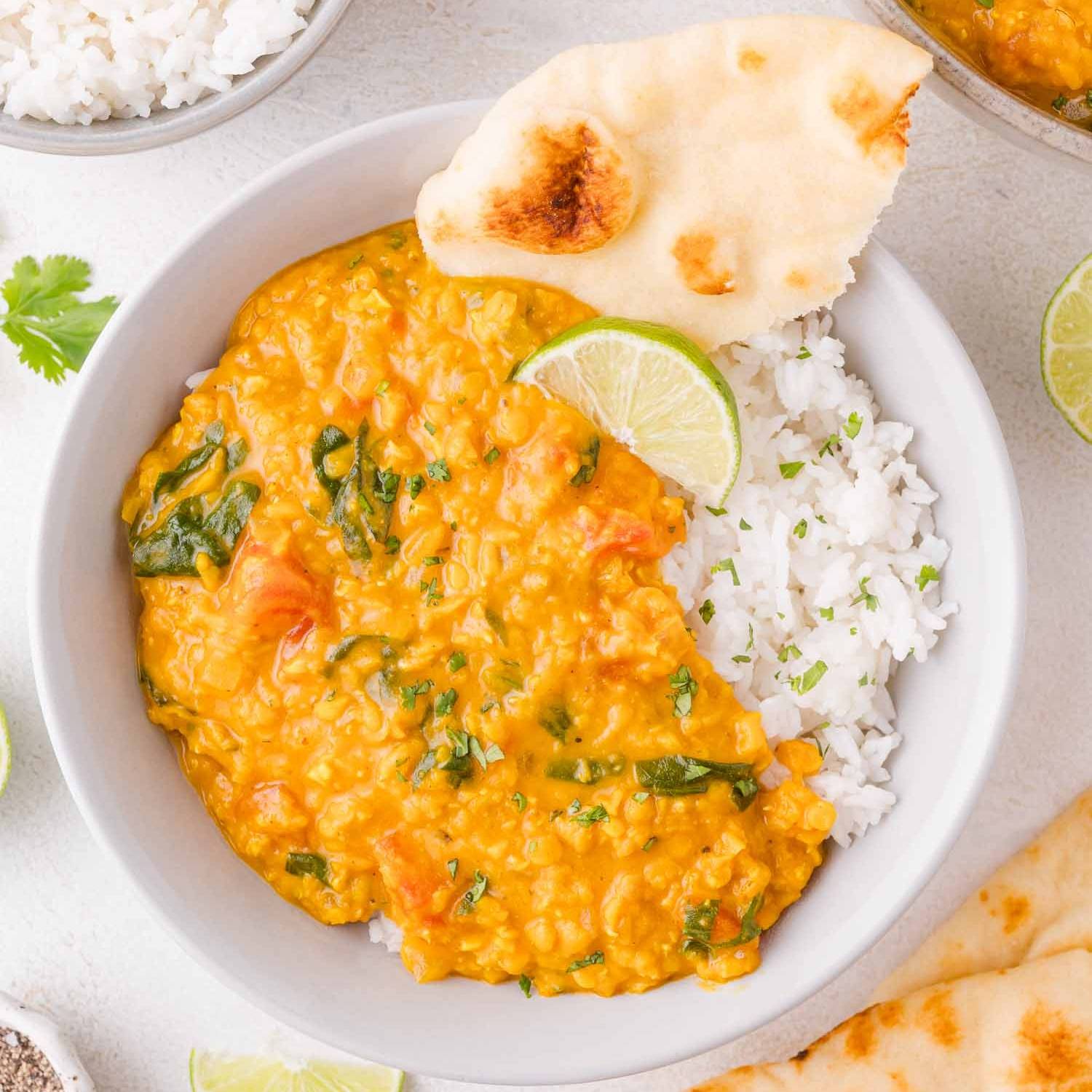 Red lentil curry in a white bowl with rice and naan.
