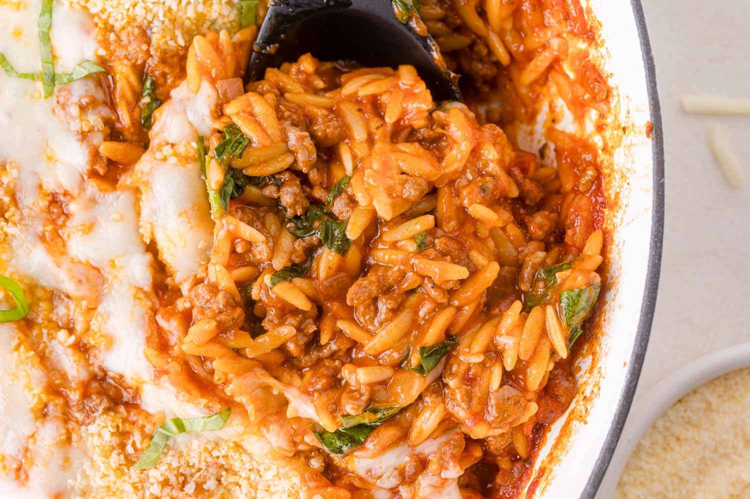 Baked orzo, topped with melted cheese and fresh basil, being scooped.