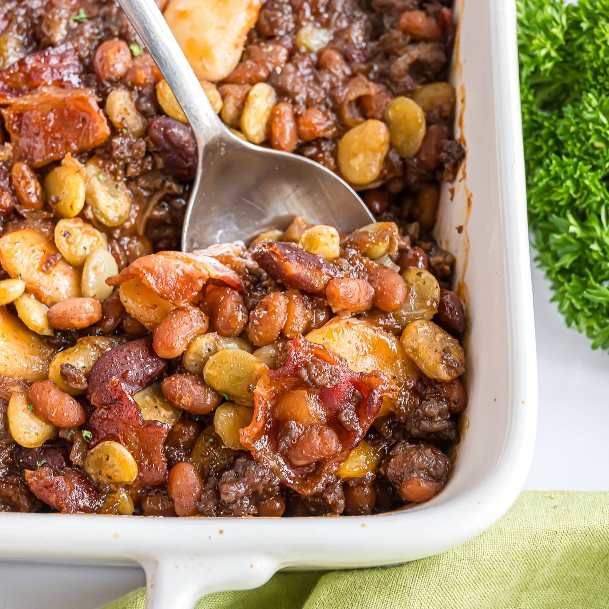 Baked beans, being scooped out of a white baking dish.