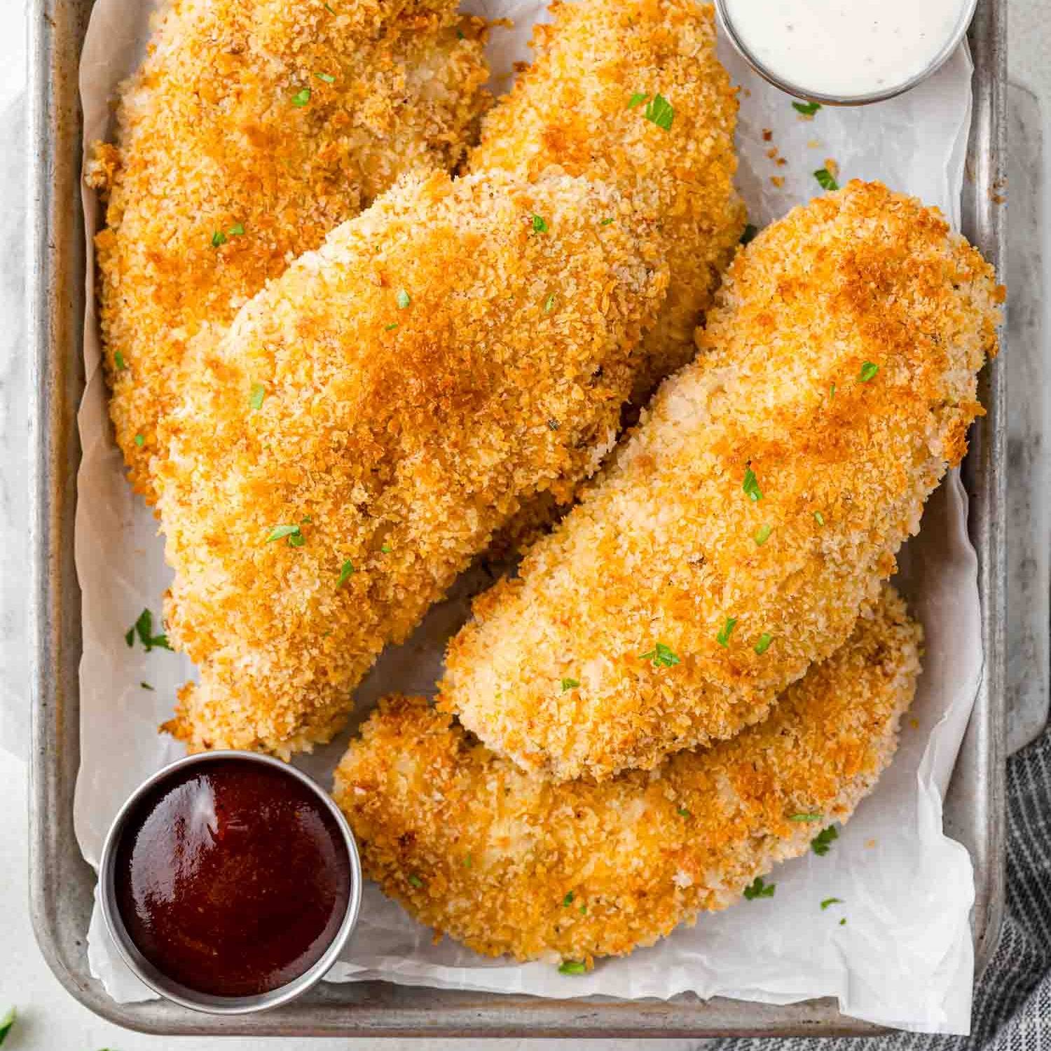 Baked chicken tenders on a small sheet pan with dipping sauces.