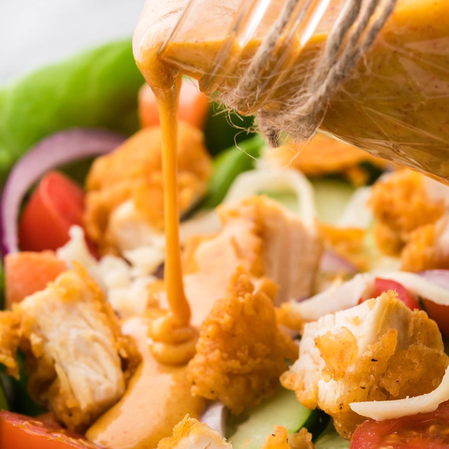 Honey mustard salad being poured on a chicken tender salad.
