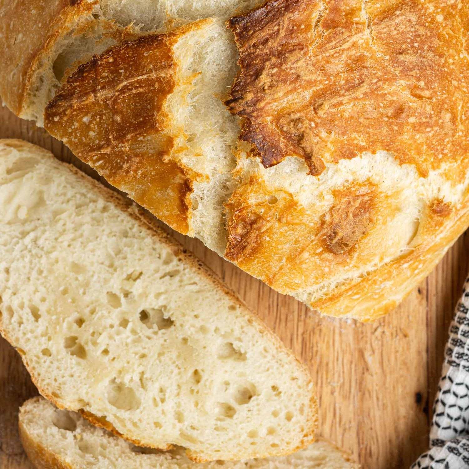 Dutch oven bread, sliced on a wood cutting board.
