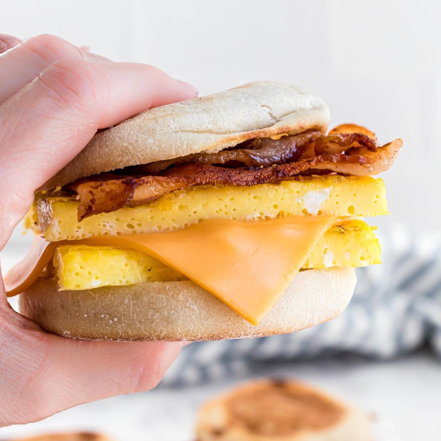 Breakfast sandwich with egg, cheese, and bacon, held in a hand.