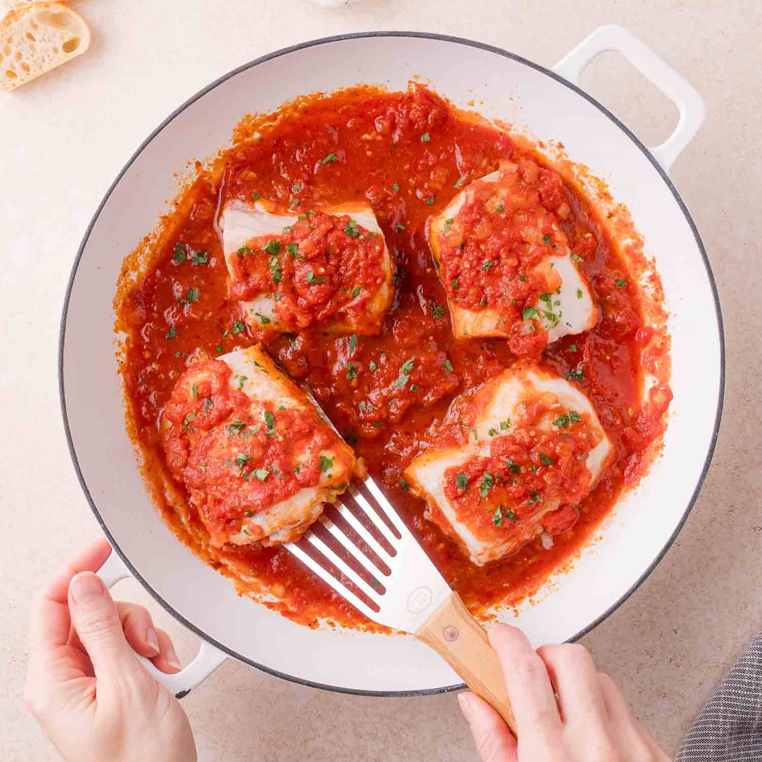 Four pieces of cod in a white pan, with tomato sauce.
