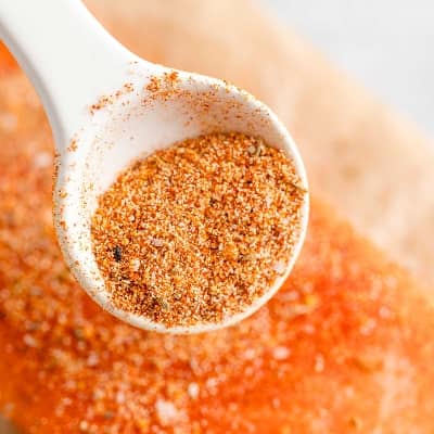 Seasoning mixture in a measuring spoon being sprinkled over salmon.