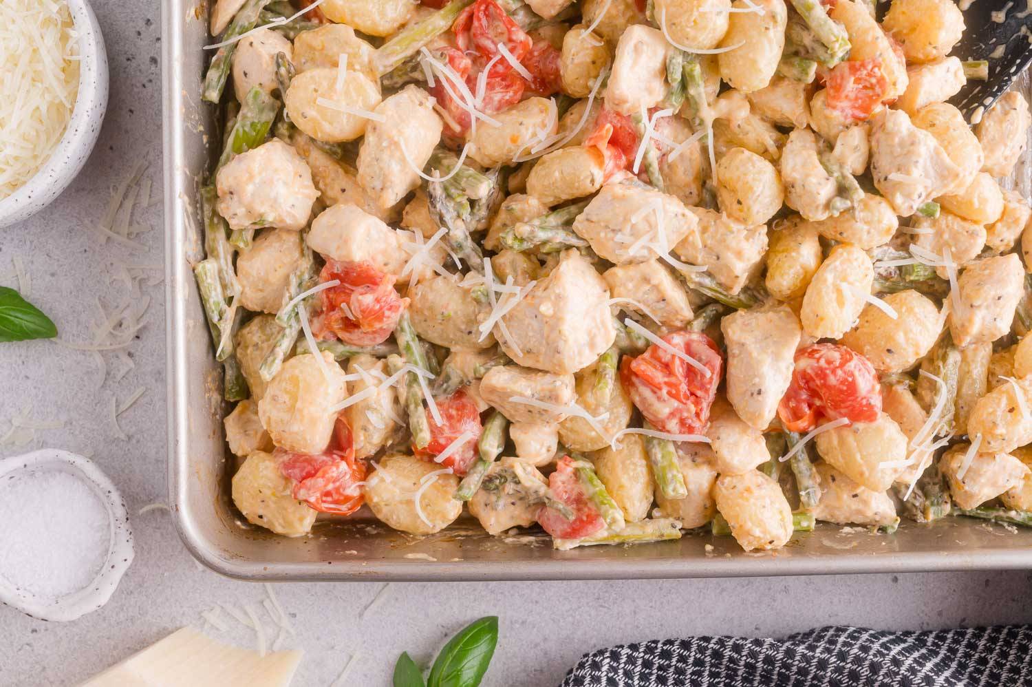 Sheet pan with gnocchi, cooked chicken, asparagus, and tomatoes, all in a creamy sauce.