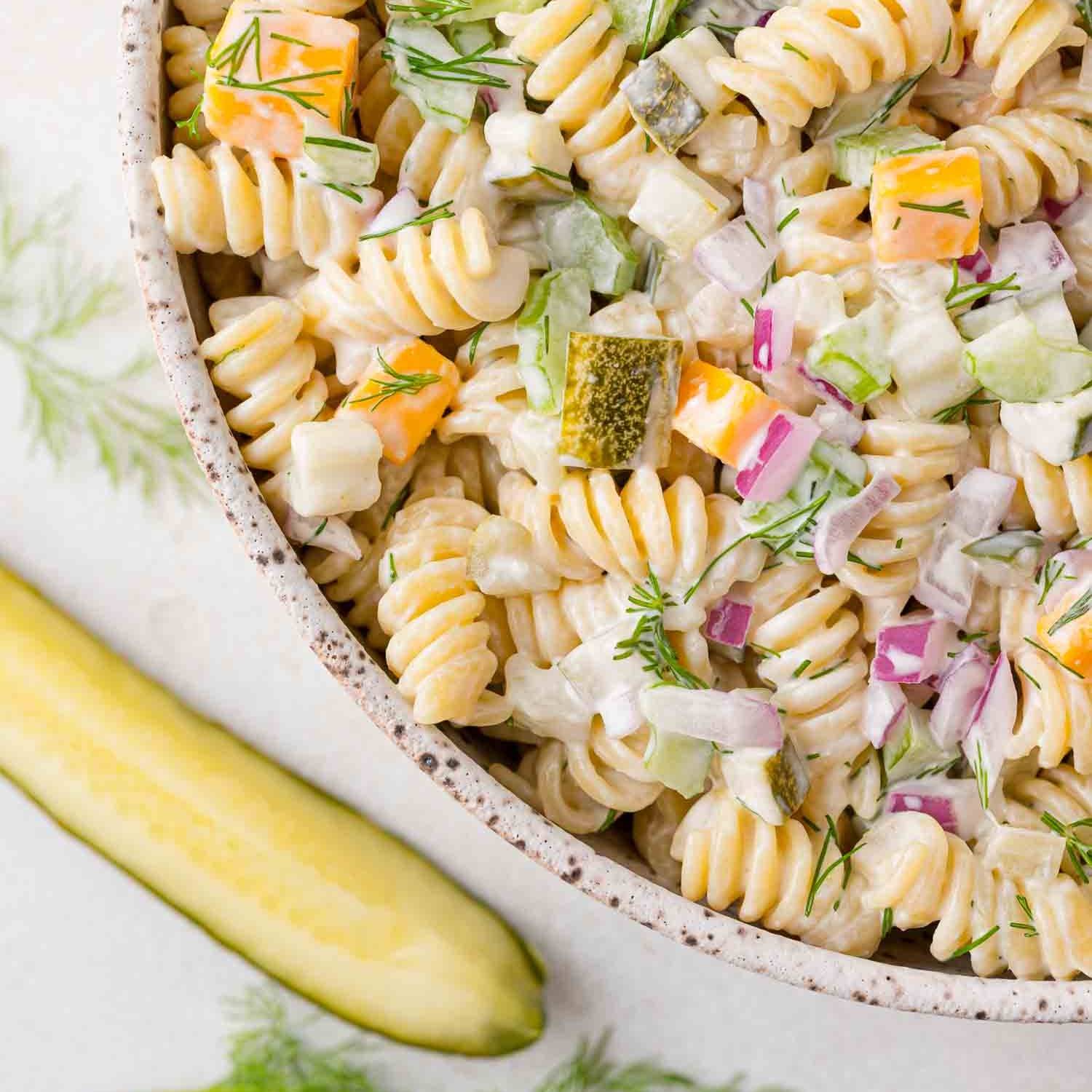 Dill pickle pasta salad with a pickle next to bowl.