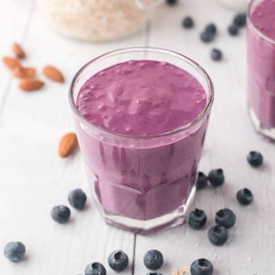 Blueberry smoothie in a short glass, surrounded by fresh blueberries and almonds.