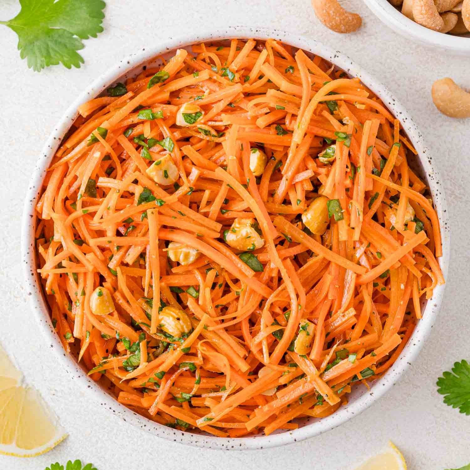 Shredded carrots in a bowl with fresh herbs and chopped nuts.