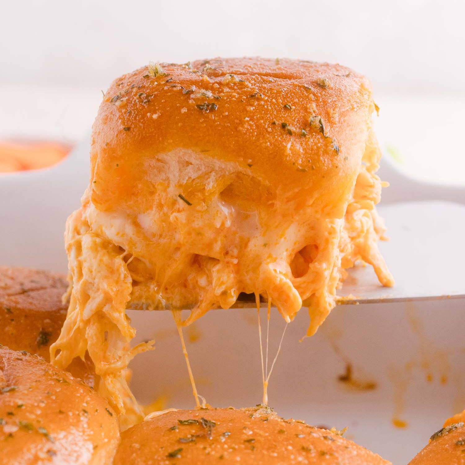 Buffalo chicken slider being lifted from a white baking dish.