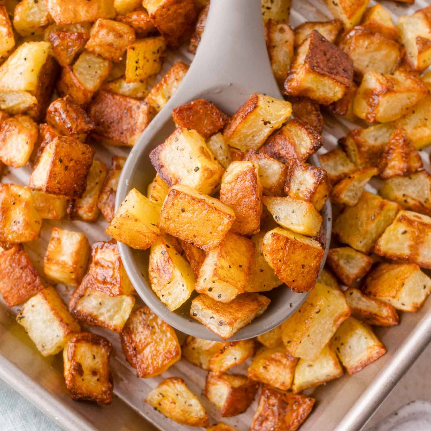 Crispy roasted potato cubes in a large serving spoon, sitting on a pan with more.