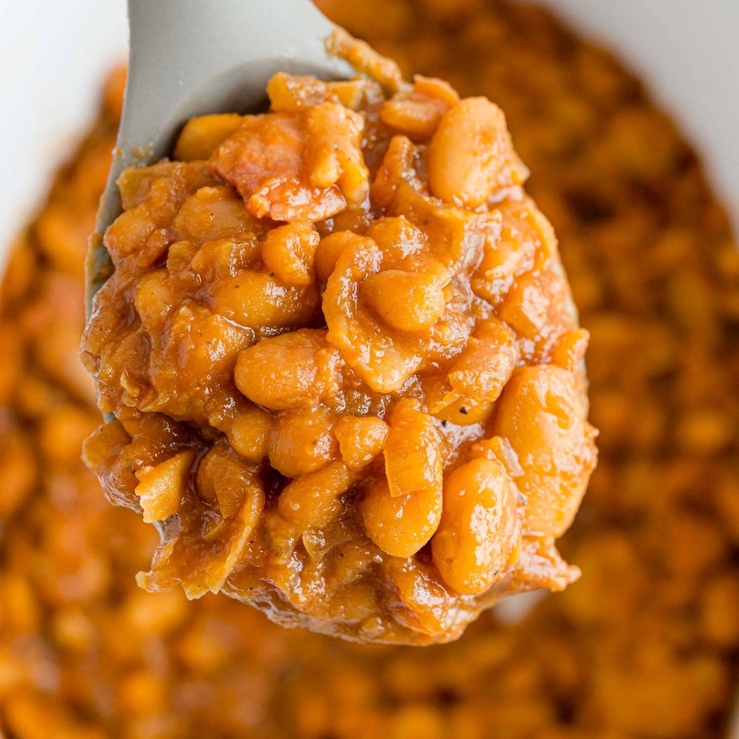 Baked beans on a spoon, being scooped from a crockpot.