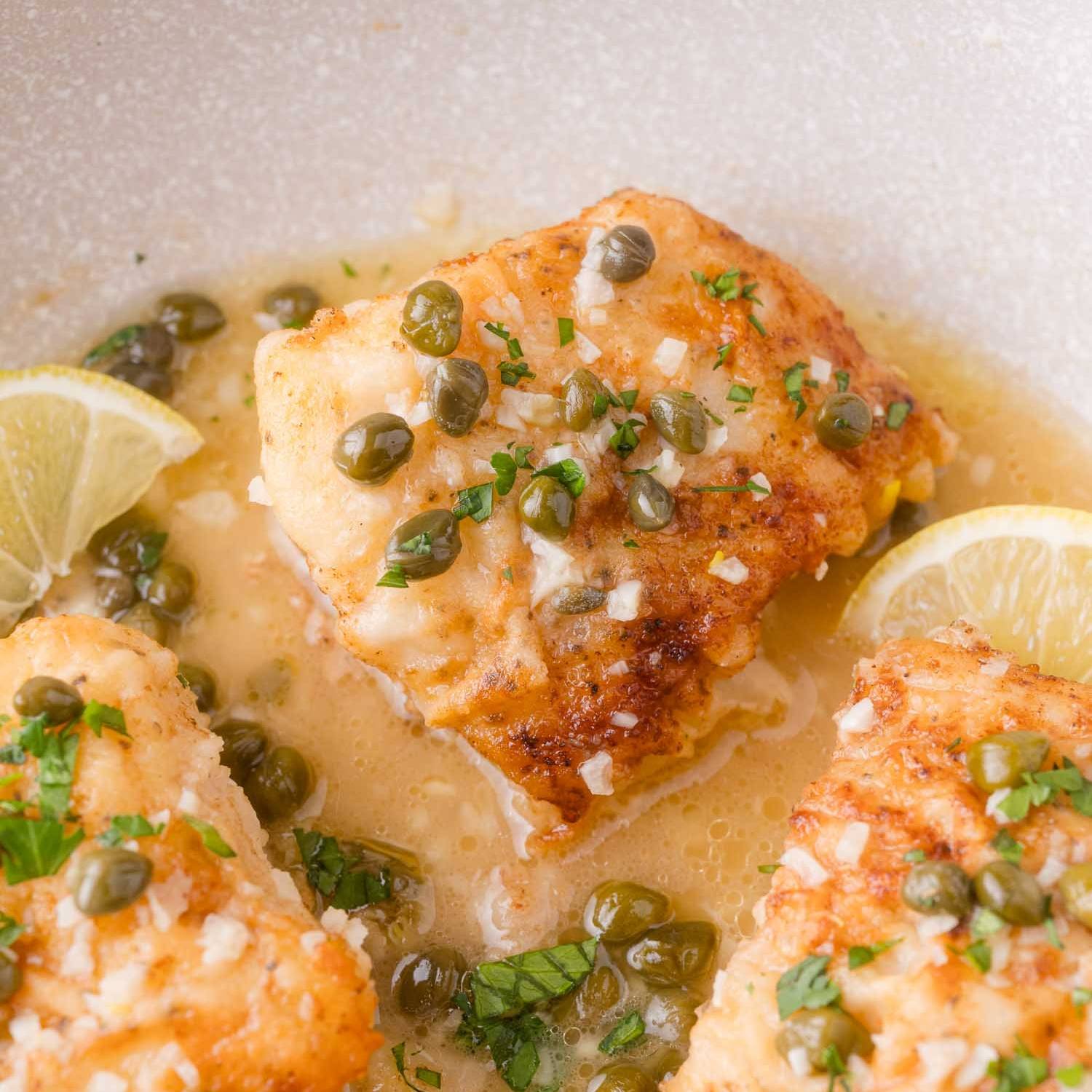Cod piccata in a white skillet, sprinkled with fresh parsley.