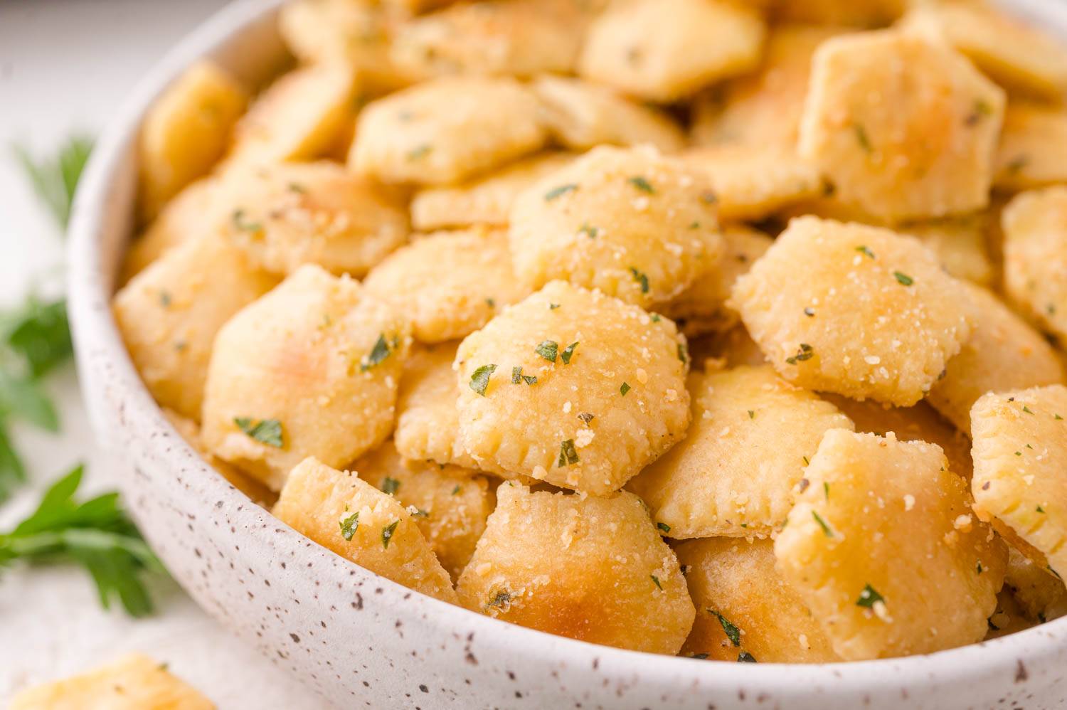 Oyster crackers with cheese and herbs, in a white speckled bowl.