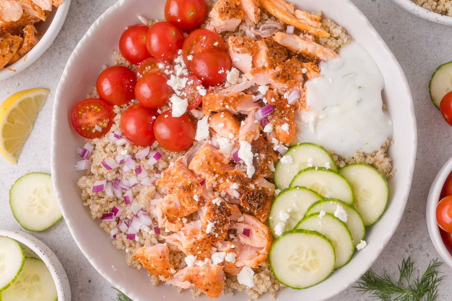 Bow with quinoa, salmon, cucumbers, onion, tomatoes, and a yogurt sauce.